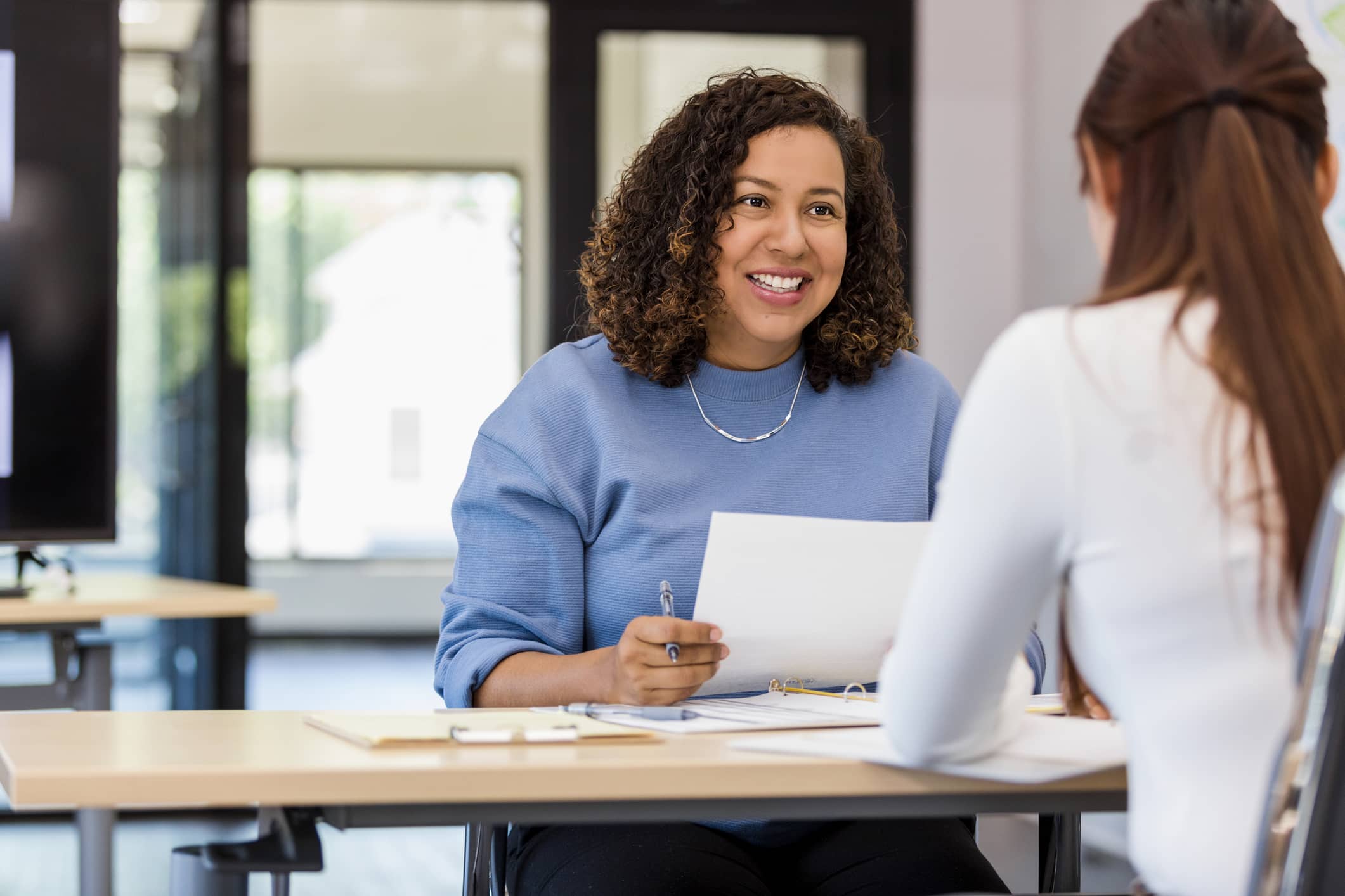Receptionist sitting at a desk with a stack of papers smiling at a client